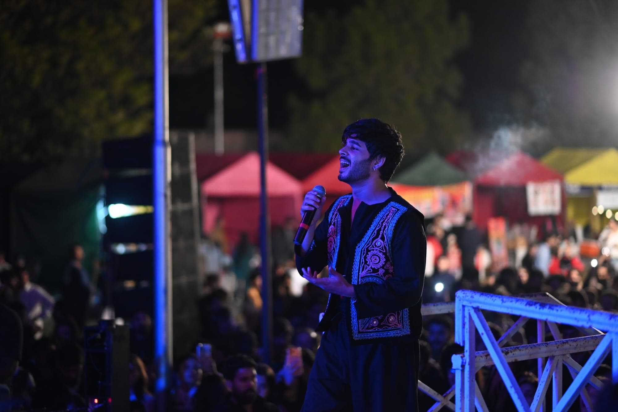 A singer in traditional embroidered attire performing among festival stalls