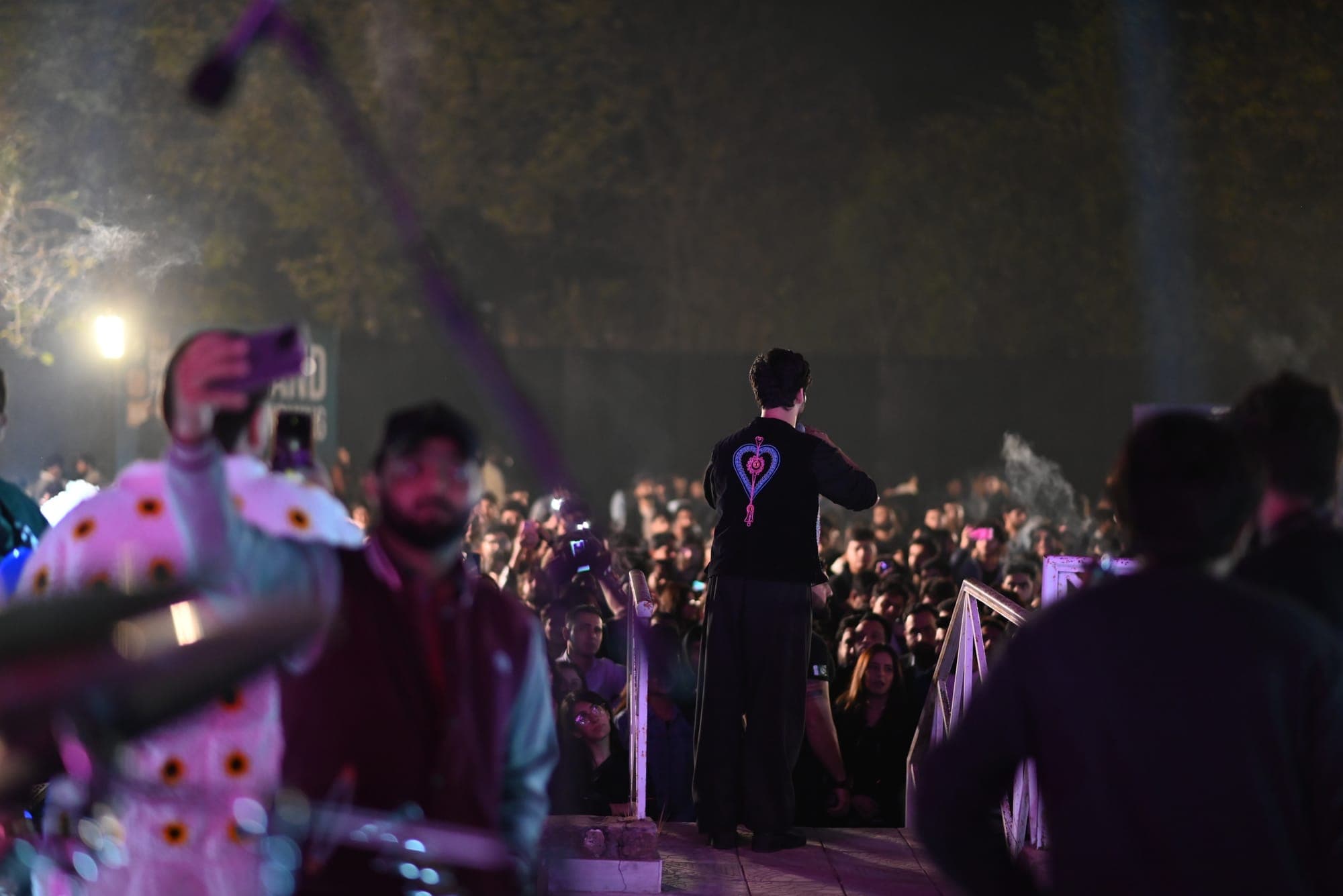 Silhouette of a performer facing a cheering crowd with phones raised